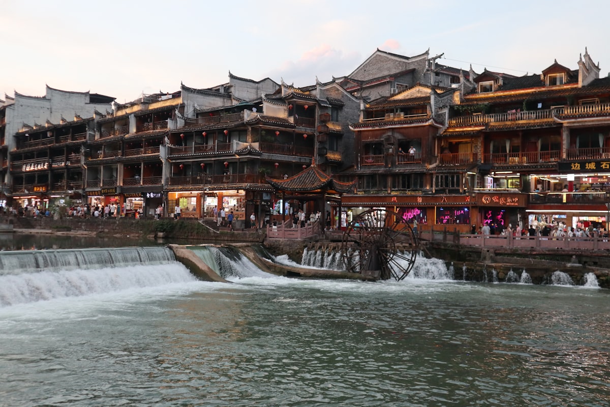Dusk over Fenghuang's stone weir and waterwheel as crowds fill the riverside street
