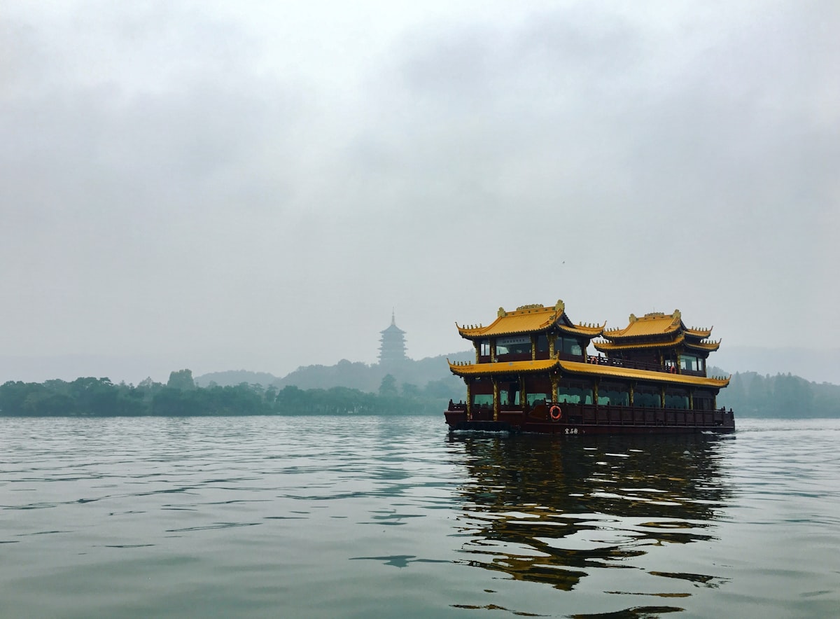 Traditional dragon boat on misty West Lake in Hangzhou with Leifeng Pagoda on the far shore