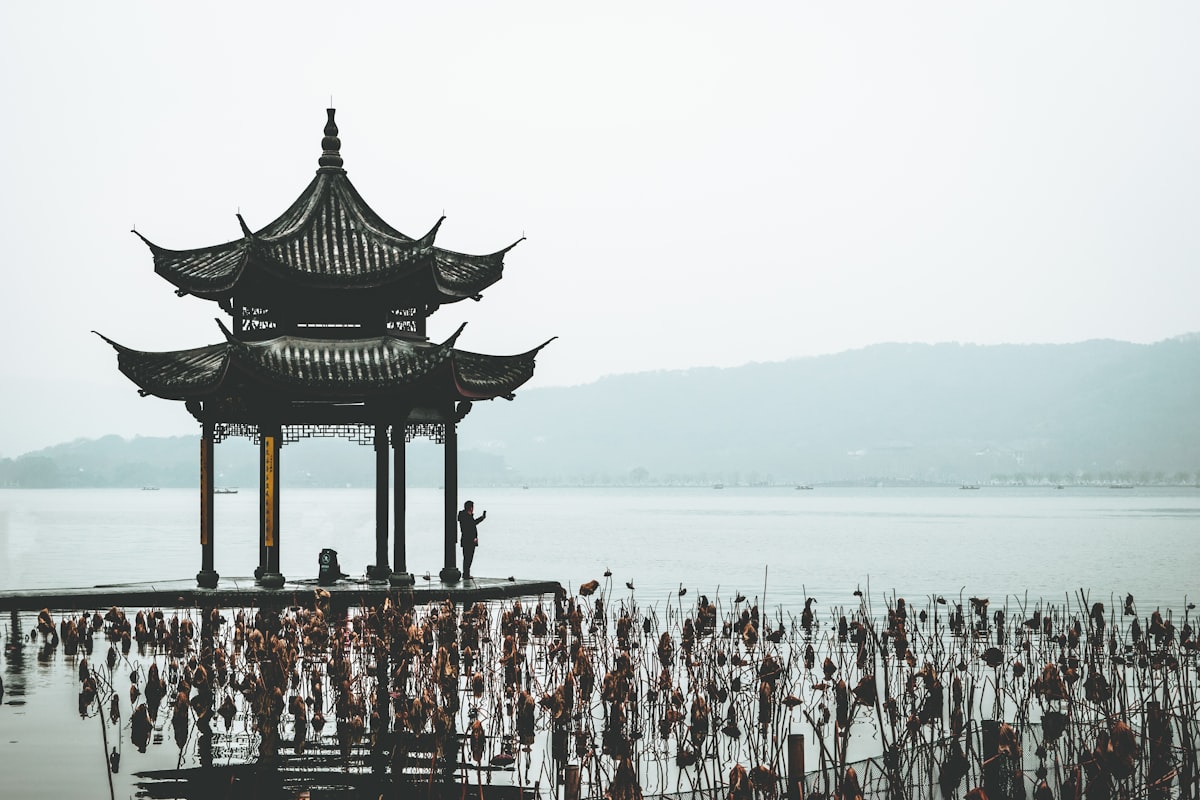 Jixian Pavilion standing over lotus stems on a hazy morning at West Lake, Hangzhou