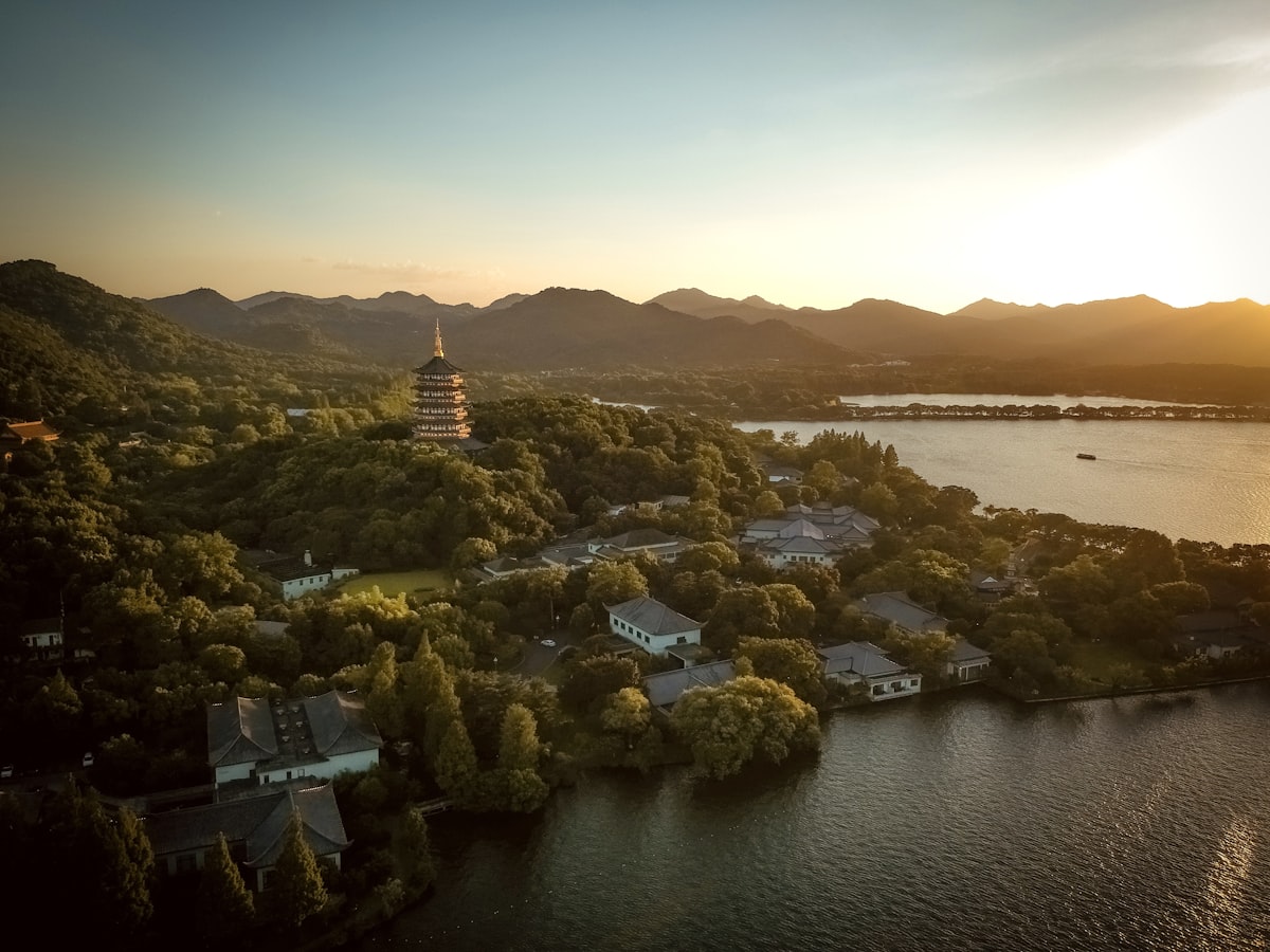 Golden-hour aerial view over West Lake in Hangzhou with a pagoda among wooded hills