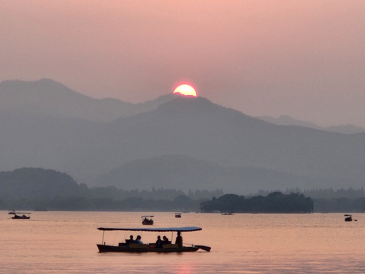 Sunset behind the hills of West Lake, Hangzhou, with a sightseeing boat on the water