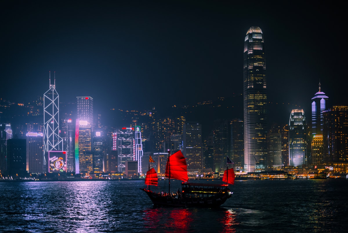 A red-sailed junk boat crosses Victoria Harbour past Hong Kong's illuminated skyline