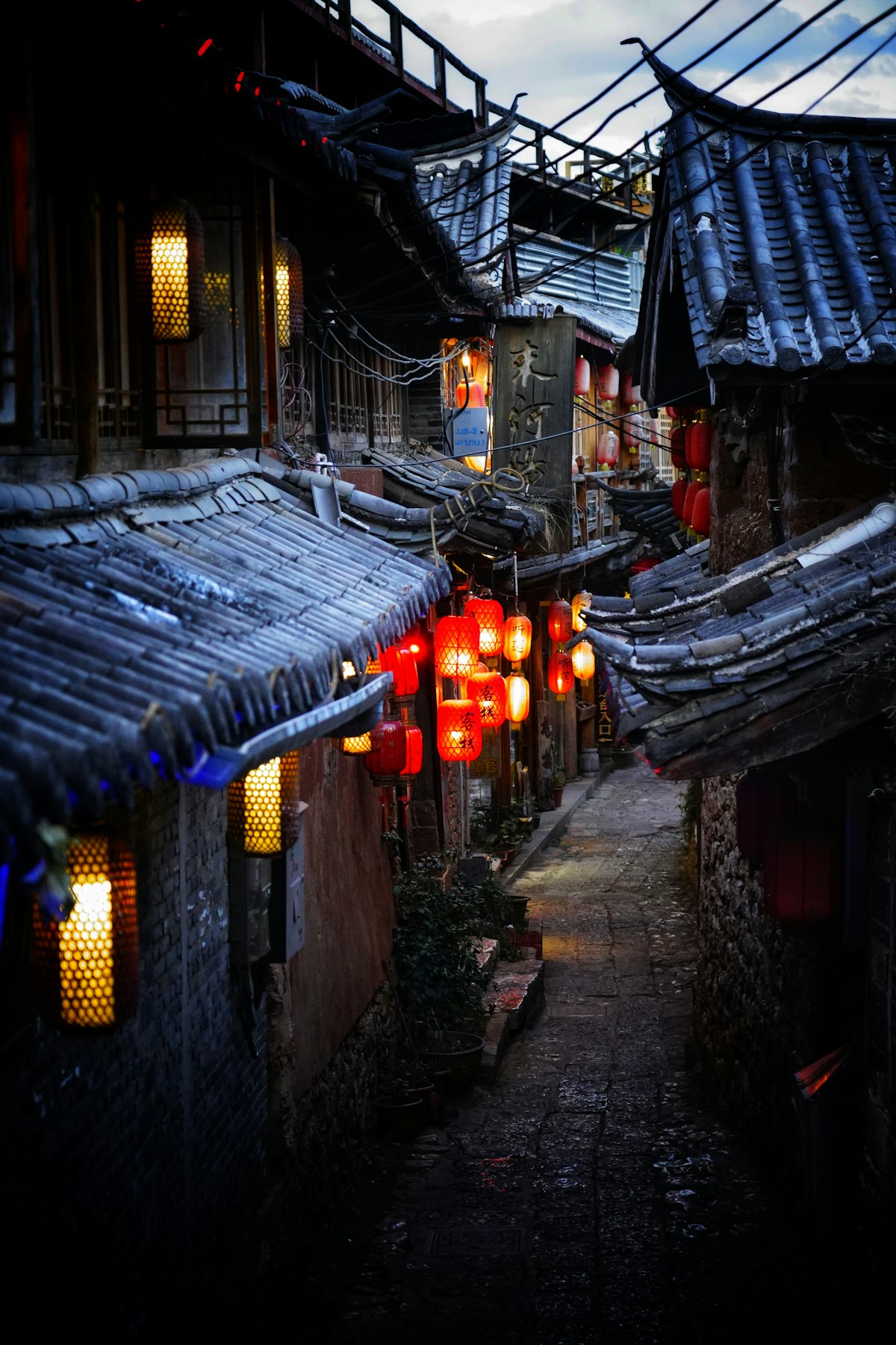 Lantern-lit lane between tiled-roof houses at night in Lijiang Old Town