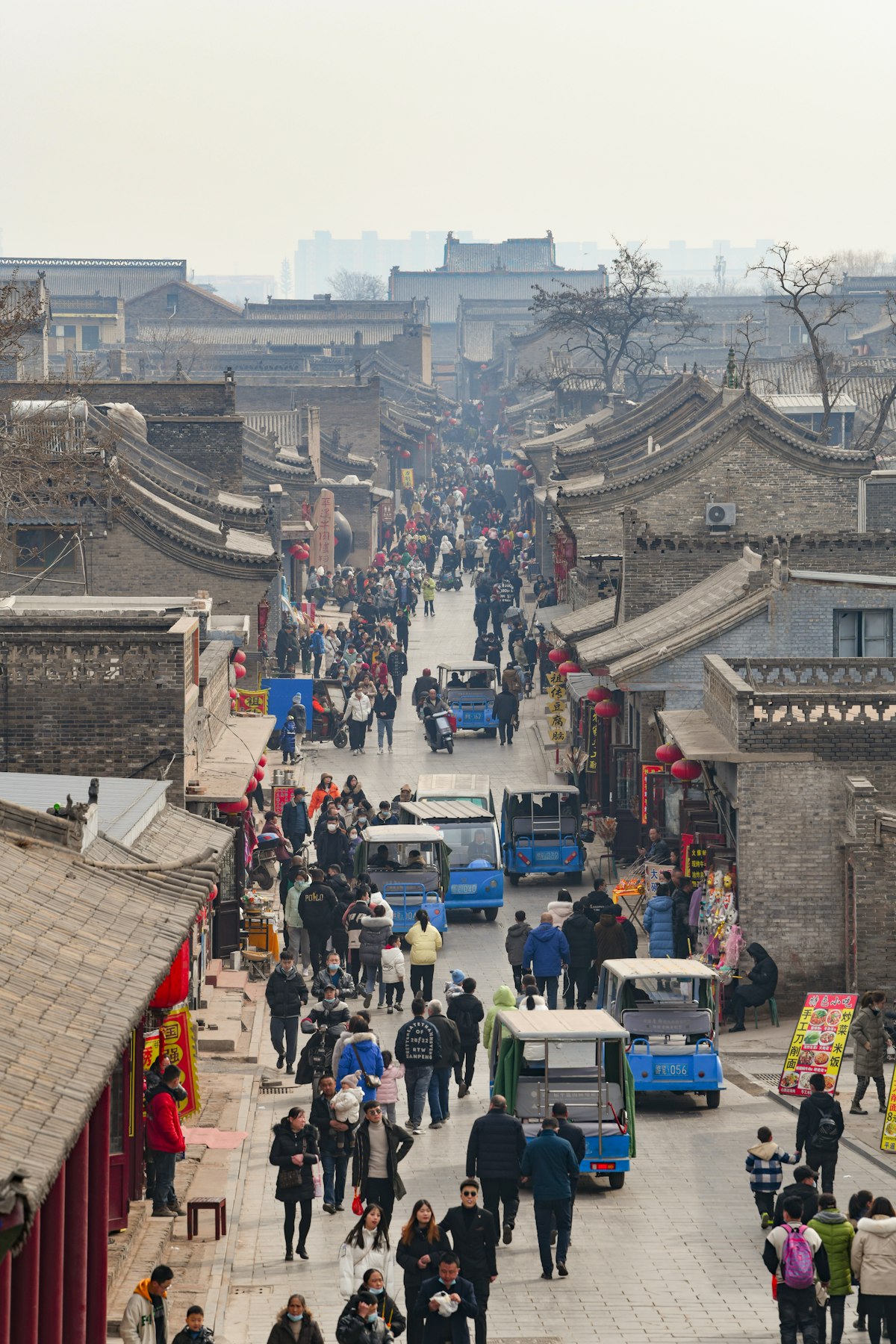 Shoppers fill a market street between grey-tiled courtyard houses in Pingyao