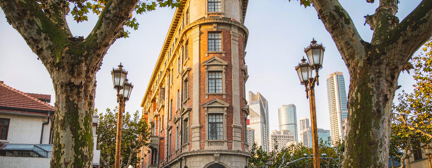 The wedge-shaped Wukang Mansion framed by plane trees, Shanghai