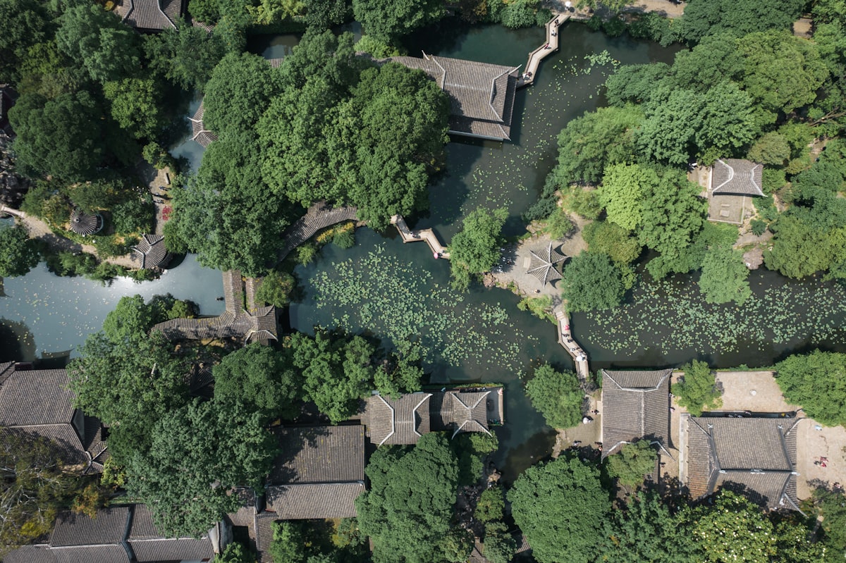 Aerial view of a classical Suzhou garden, its tiled pavilion roofs winding around a lotus pond