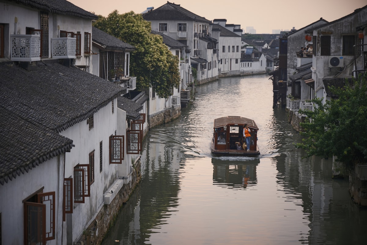A sightseeing boat glides down a quiet canal between whitewashed houses in Suzhou