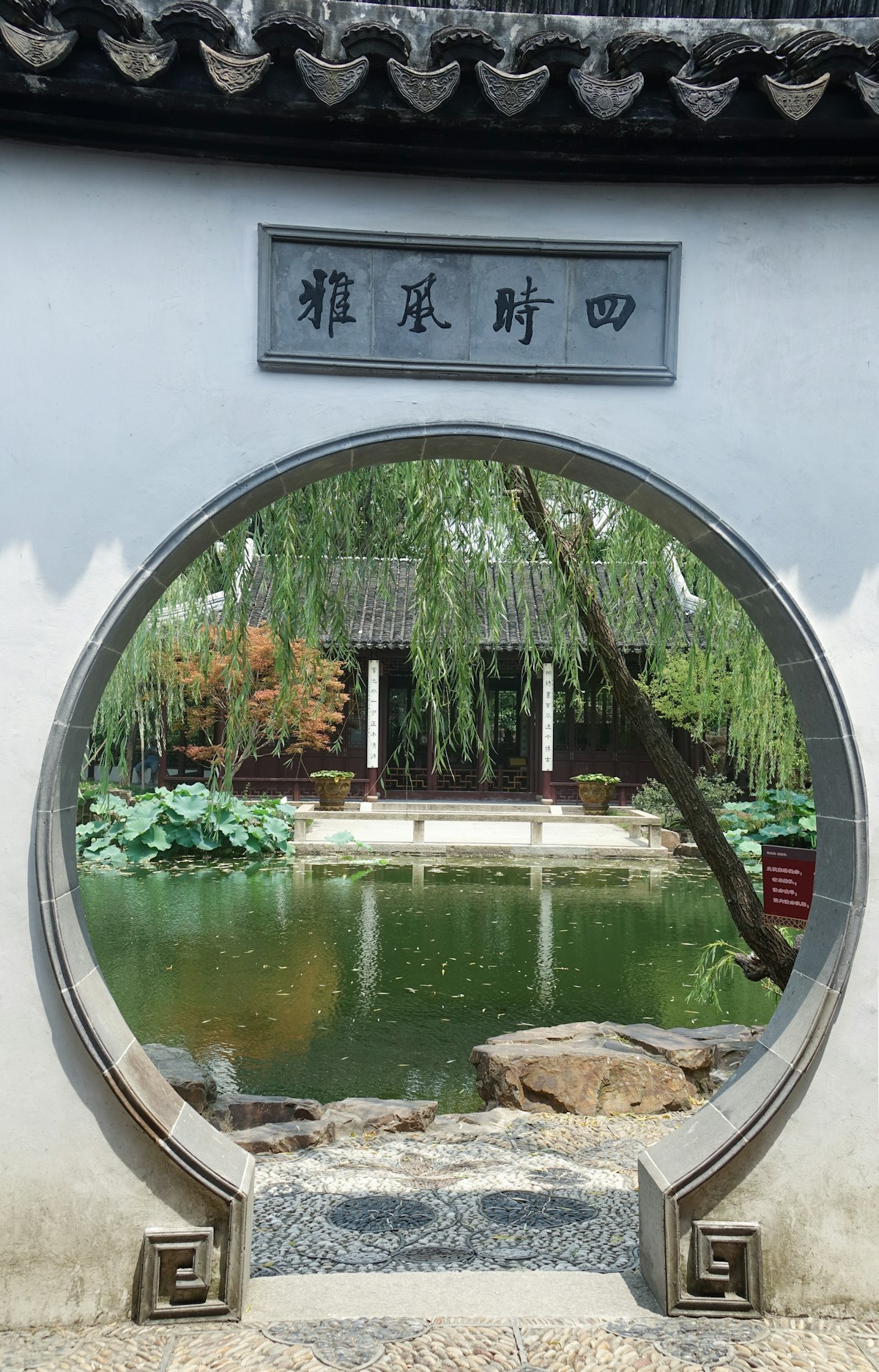 Moon gate opening onto a pond and willow tree in a Suzhou classical garden