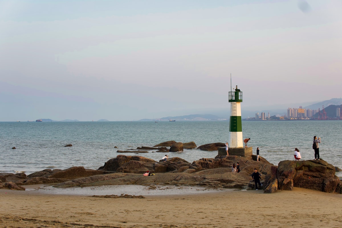 Visitors gather by a small lighthouse on a rocky beach along Xiamen's coast