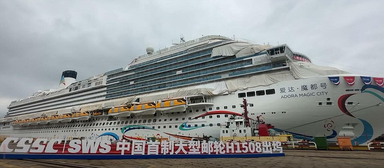 The Adora Magic City, China's first domestically built large cruise ship, at sea with its white and blue hull and red funnel.