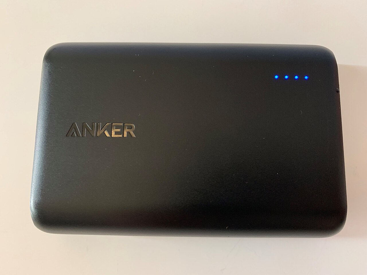 A black Anker power bank with its charge-indicator lights lit, lying on a desk.