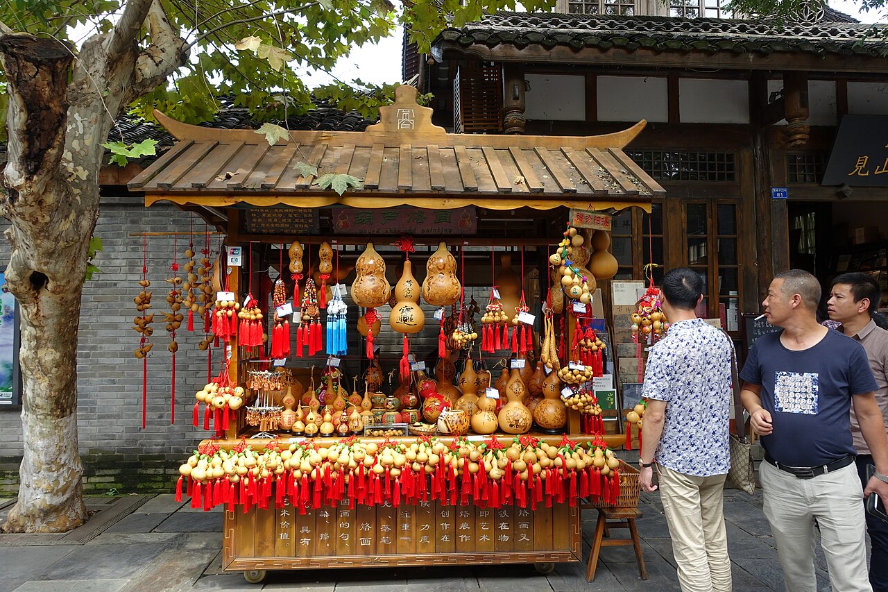 A souvenir cart hung with painted gourds and red tassels in front of a grey-brick shopfront in Kuanzhai Alley.