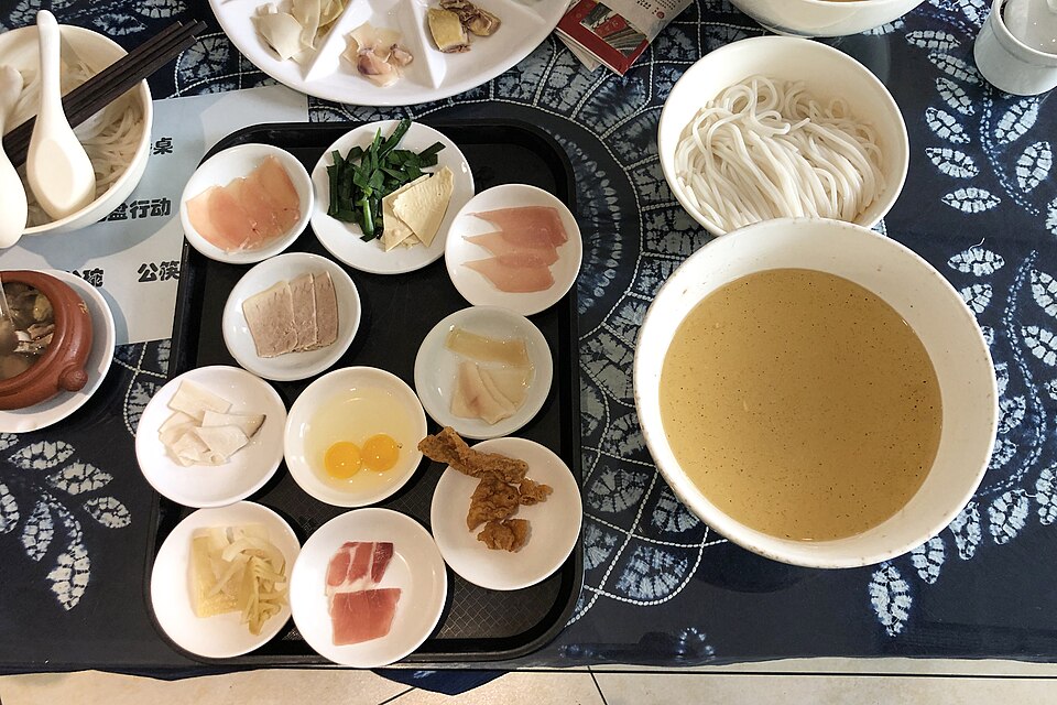 A bowl of crossing-the-bridge rice noodles with side plates, Yunnan