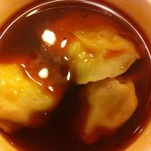 Long chaoshou wontons in a dark bowl of red chilli oil