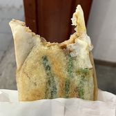 A congbaohui pancake folded in paper, spring onion showing through the crust