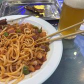 A plate of laghman hand-pulled noodles with a glass of beer