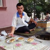 A baker beside his tandoor with trays of samsa pies
