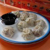 A plate of steamed momo dumplings with a dish of dipping sauce