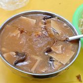 A bowl of Luoyang hulatang, thick and brown, with the spoon standing in it