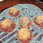 Five xiaolongbao in a bamboo steamer, pleated at the top