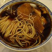 A bowl of aozao noodles in dark broth with the topping laid over them