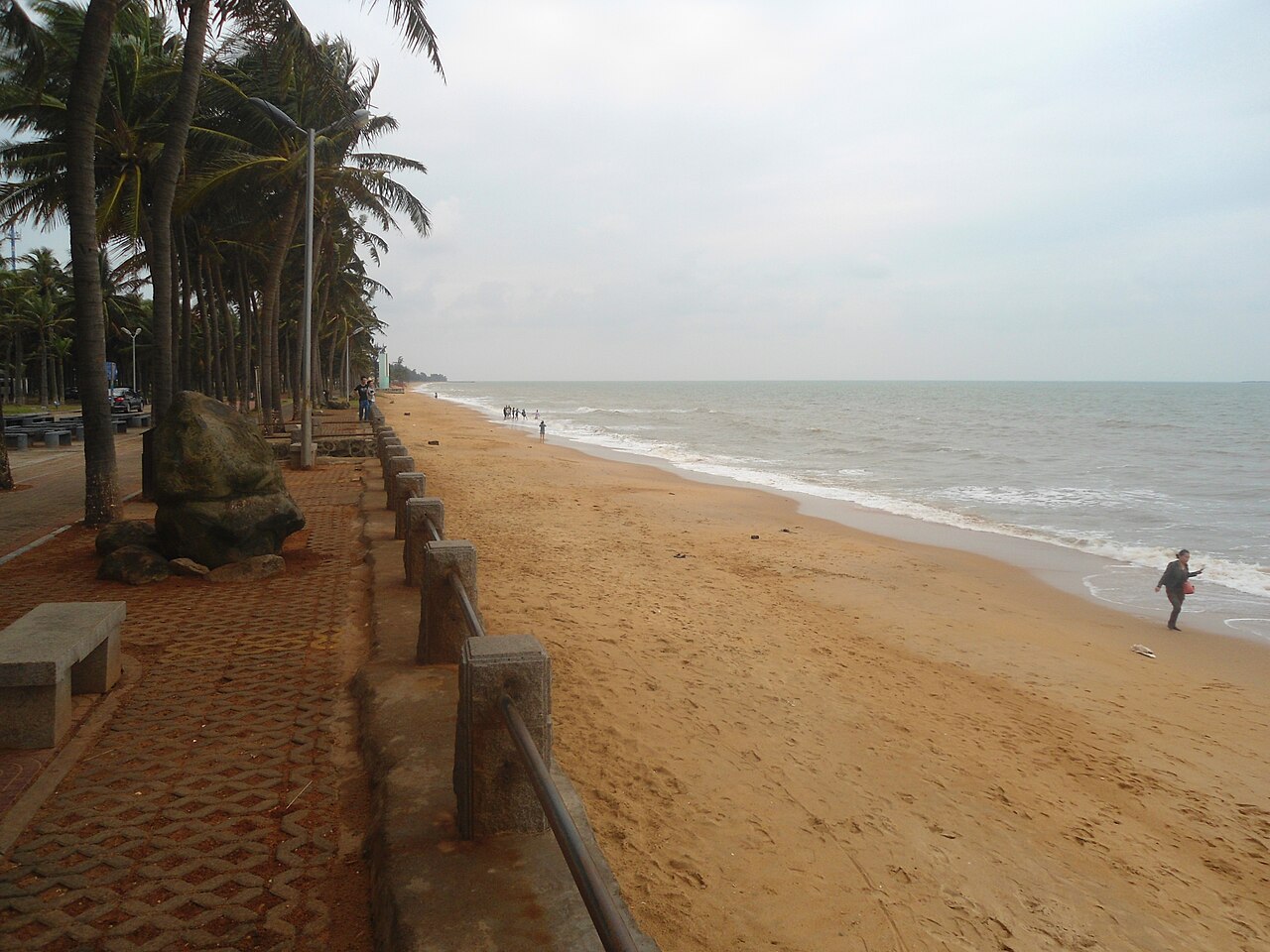 Palm trees lining the golden sand of Holiday Beach, a lone walker by the calm sea.
