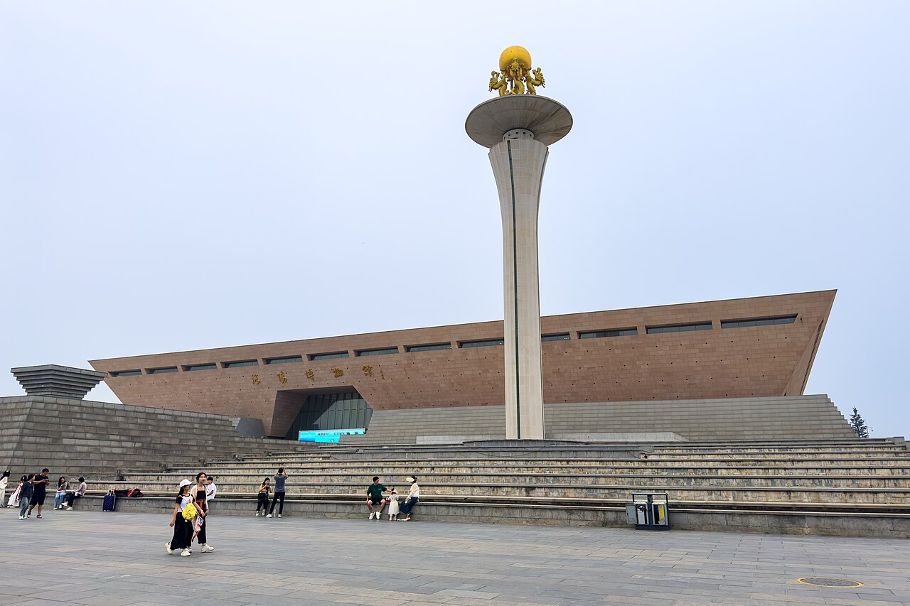 The trapezoidal hall of the Luoyang Museum behind its steps, a gold-topped column in front