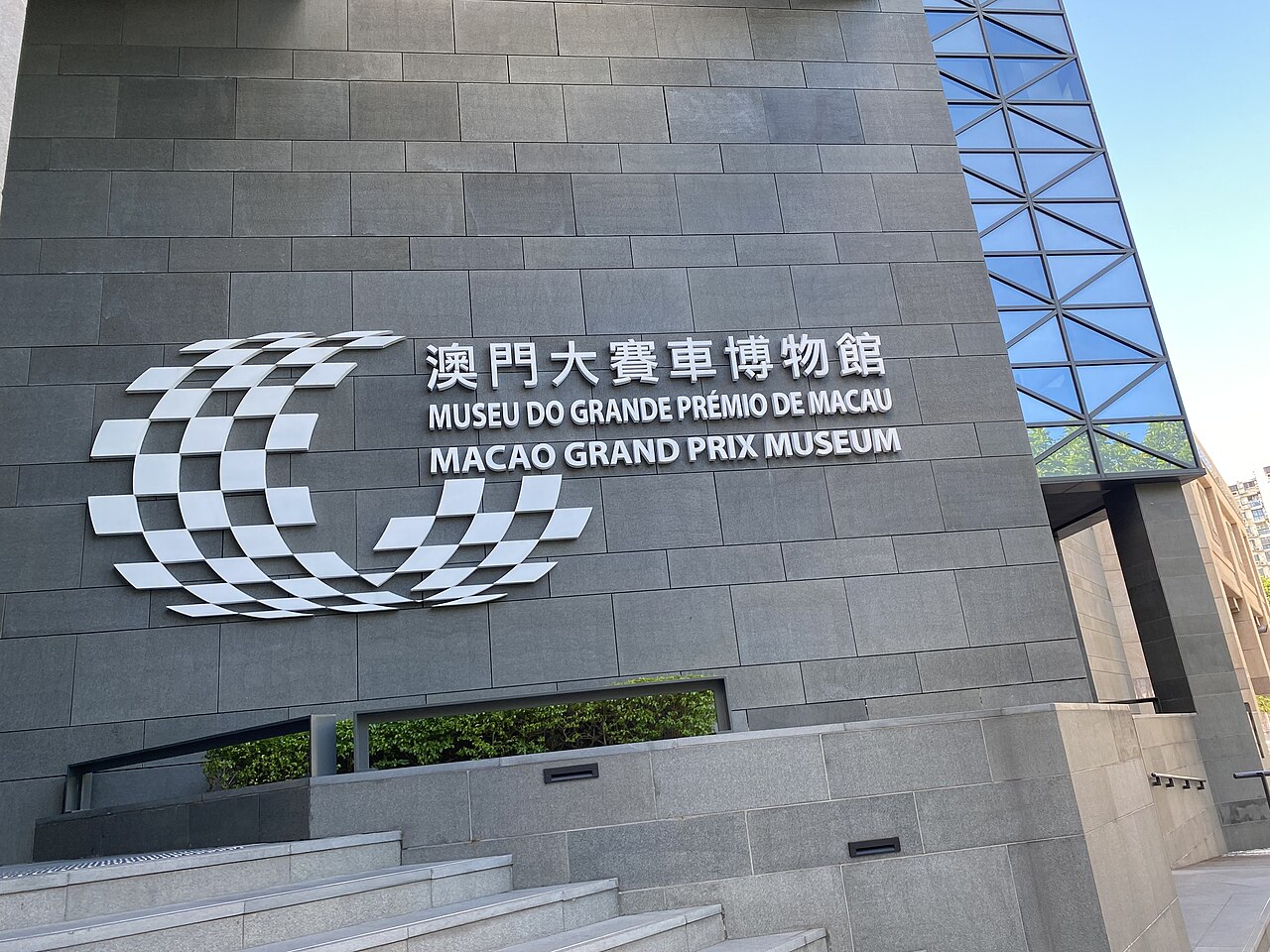 The grey stone frontage of the Macao Grand Prix Museum, with a chequered-flag emblem and the museum's name in Chinese, Portuguese and English.