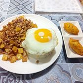 Minced pork and fried potato cubes beside a fried egg over rice, with two golden croquettes on side dishes on a patterned tile table.