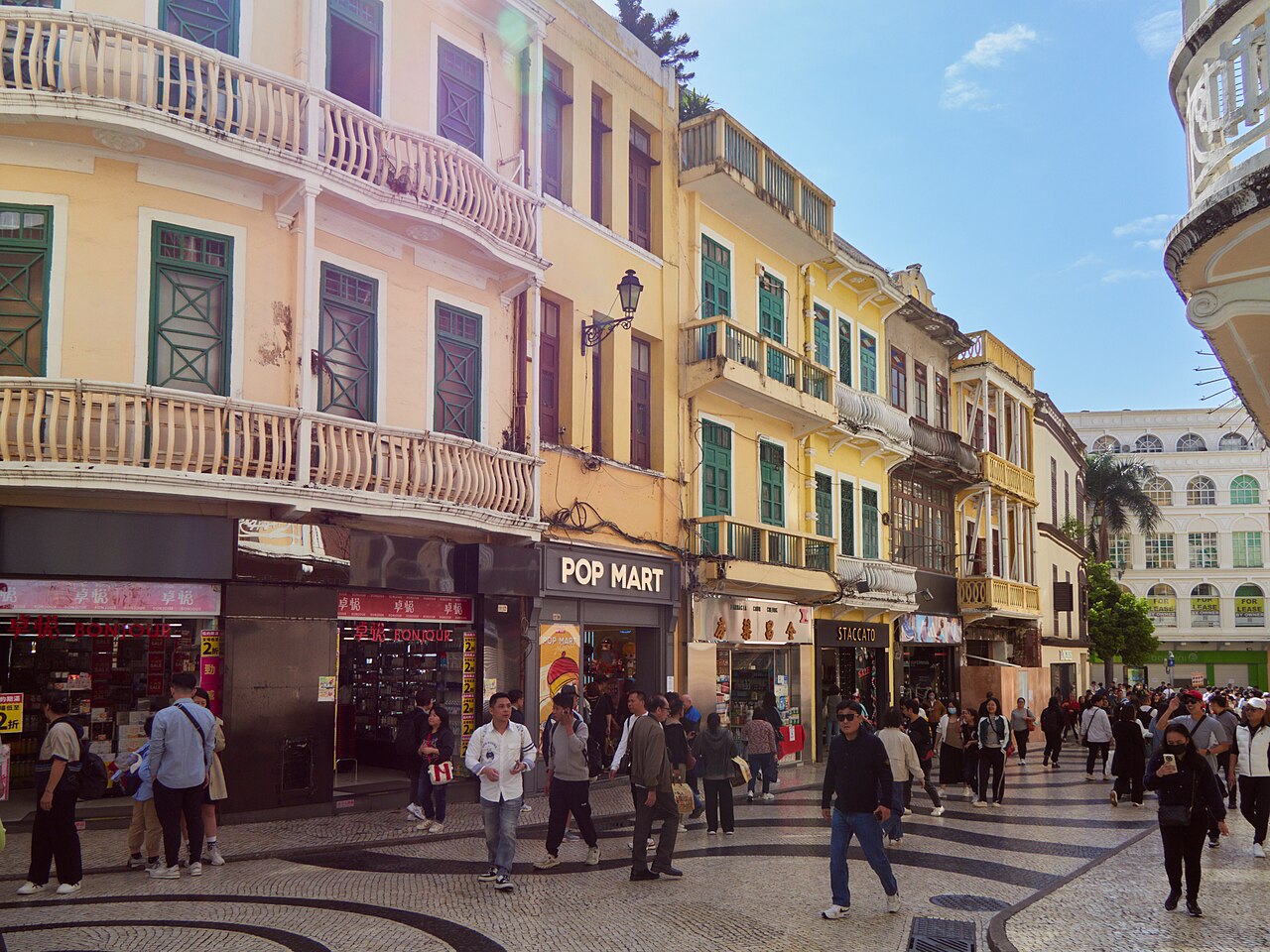 Crowds cross the black-and-white wave paving of Senado Square, past pastel shophouses with green shutters and iron balconies.