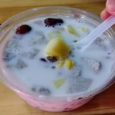 A takeaway bowl of qingbuliang: coconut milk with red beans, red dates, dragon fruit and mango, eaten with a plastic spoon.
