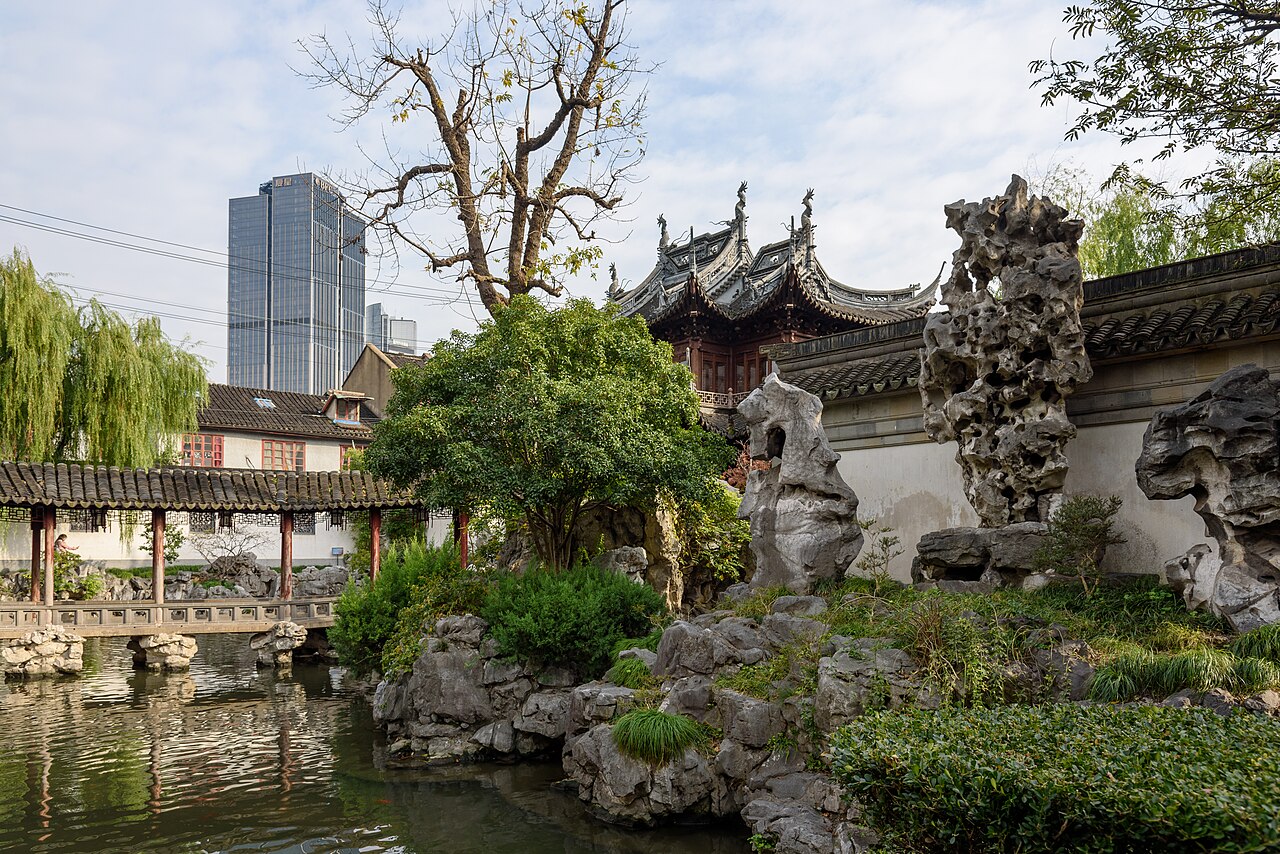 Rockeries, a pond and pavilion roofs inside Yu Garden, a modern tower rising behind