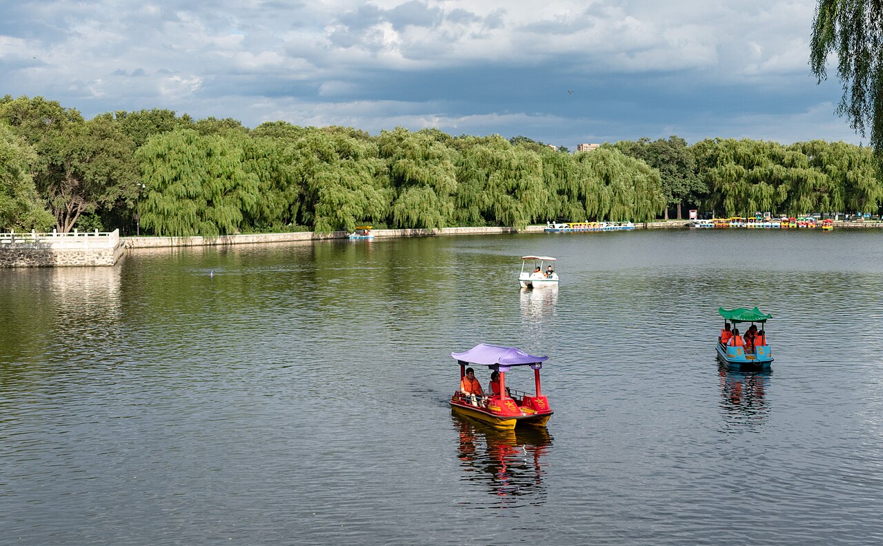 Pedal boats drifting on Beiling Park's lake under a wide sky, willow trees lining the shore.