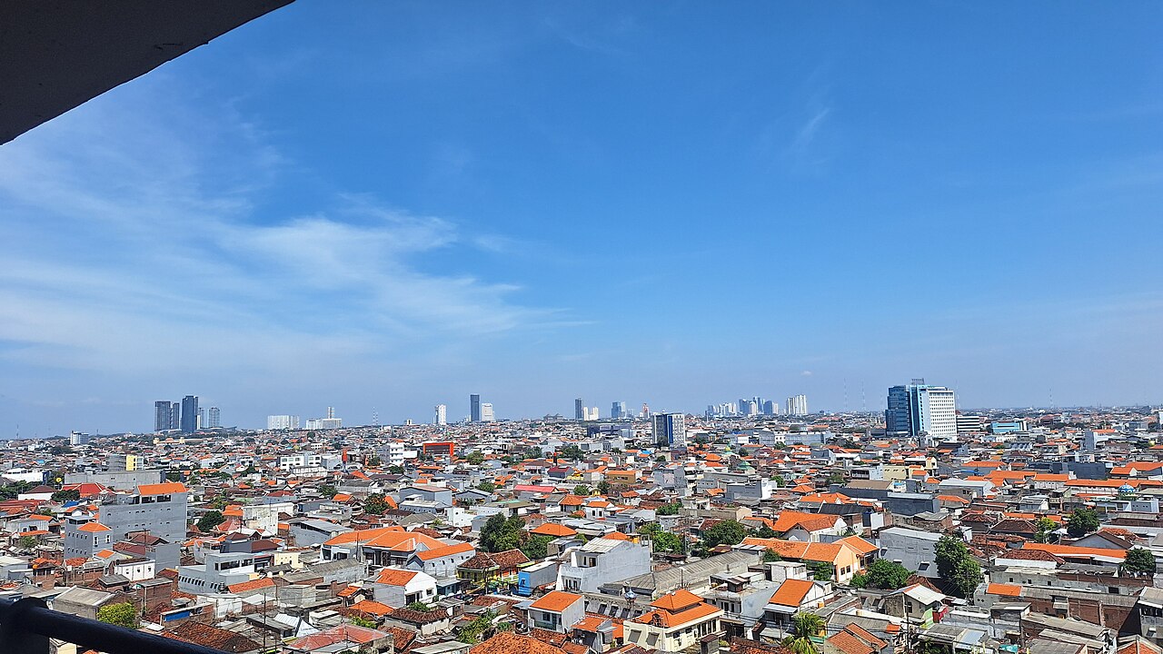 The Surabaya skyline with high-rise towers and the crescent-shaped Al Akbar mosque minarets visible in the distance.