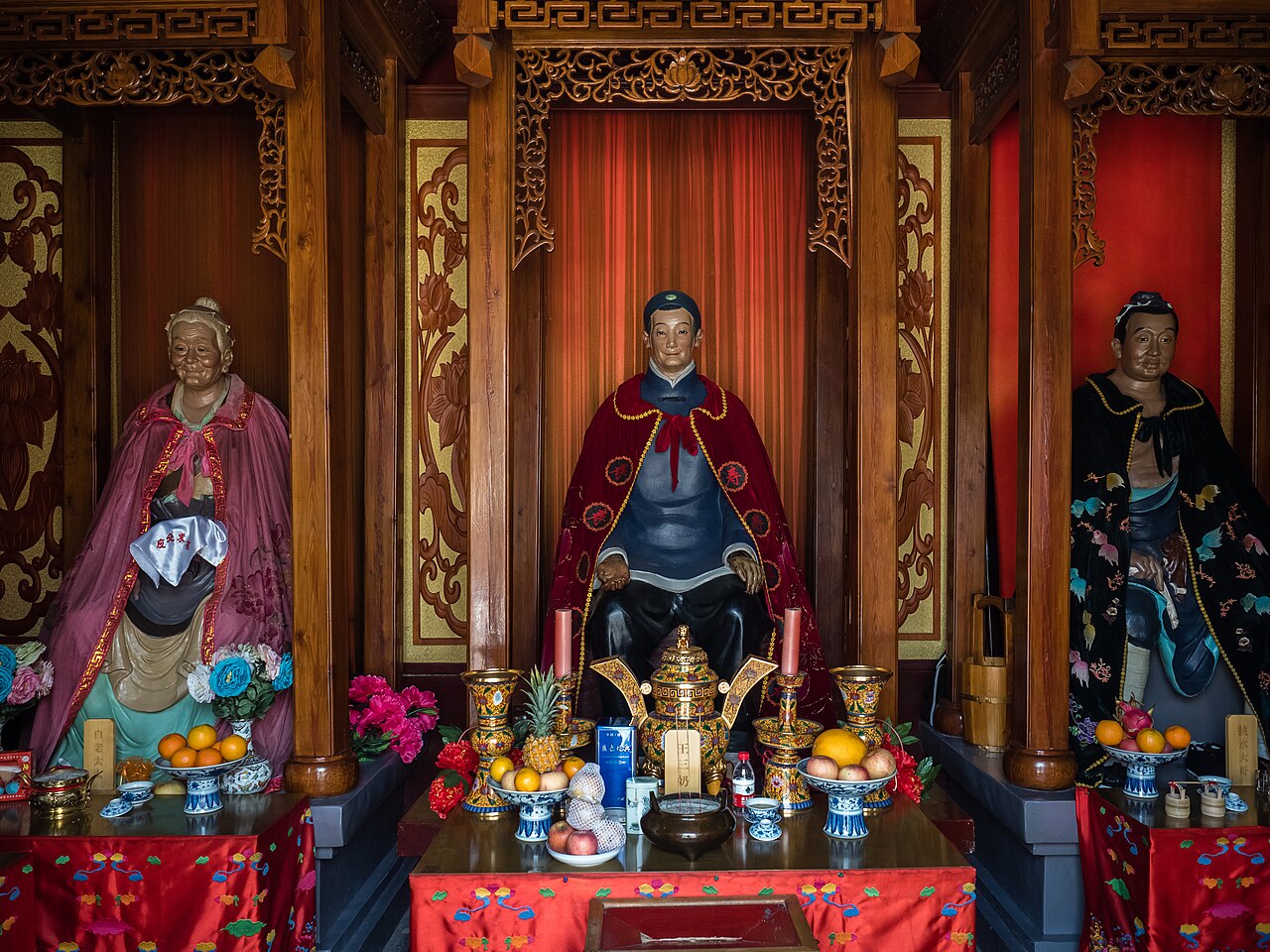 The altar of Tianhou Palace with painted deity statues and offerings under carved wooden canopies.