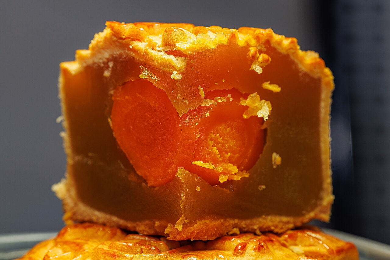 A Cantonese lotus-seed-paste mooncake cut open to show a whole salted egg yolk at its centre