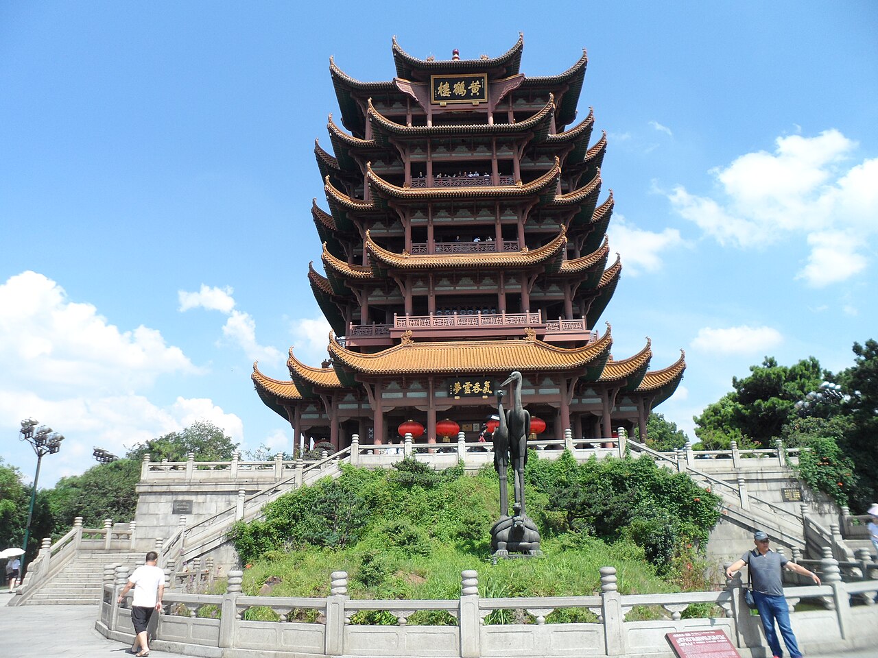 The five-tiered Yellow Crane Tower seen head on, golden tiled eaves at every level, a black plaque under the top roof, visitors along the balconies and red lanterns hung below