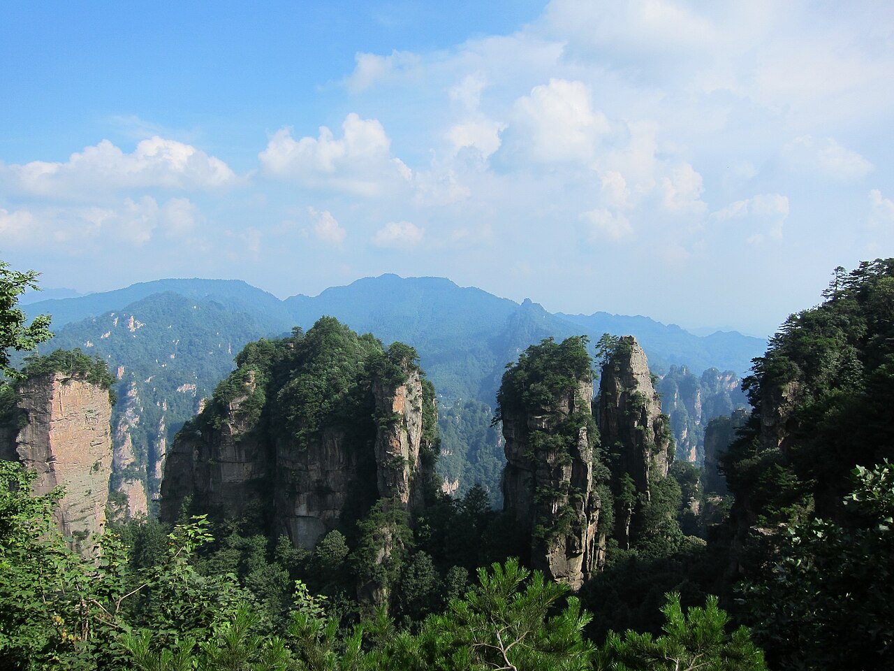 Tall quartz-sandstone peaks standing above dense green forest under a bright, partly clouded sky.