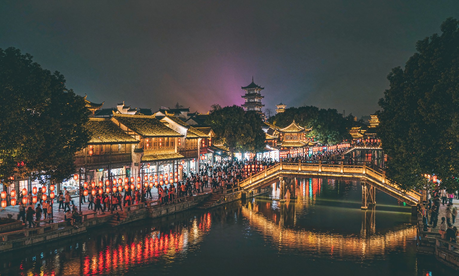 An old Chinese water town lit up at night, with visitors walking along the canal