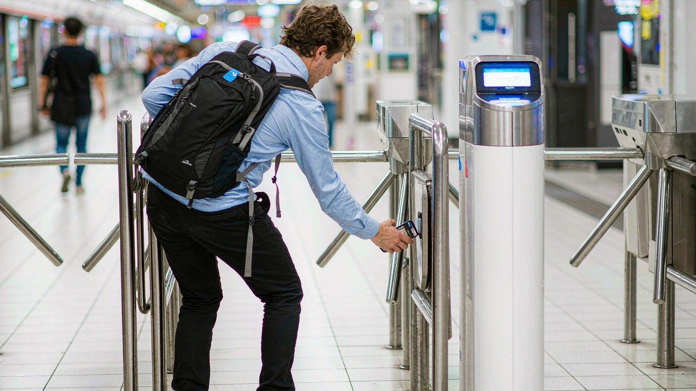 A passenger holds a smartphone at a metro gate in a modern Chinese subway station