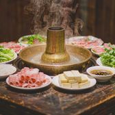 A plate of hand-cut lamb rolled for the pot, beside a copper hotpot