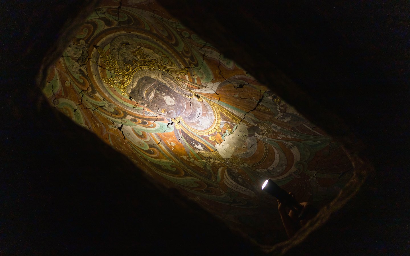 A hand lamp lighting a 600-year-old gilded Buddhist mural in darkness