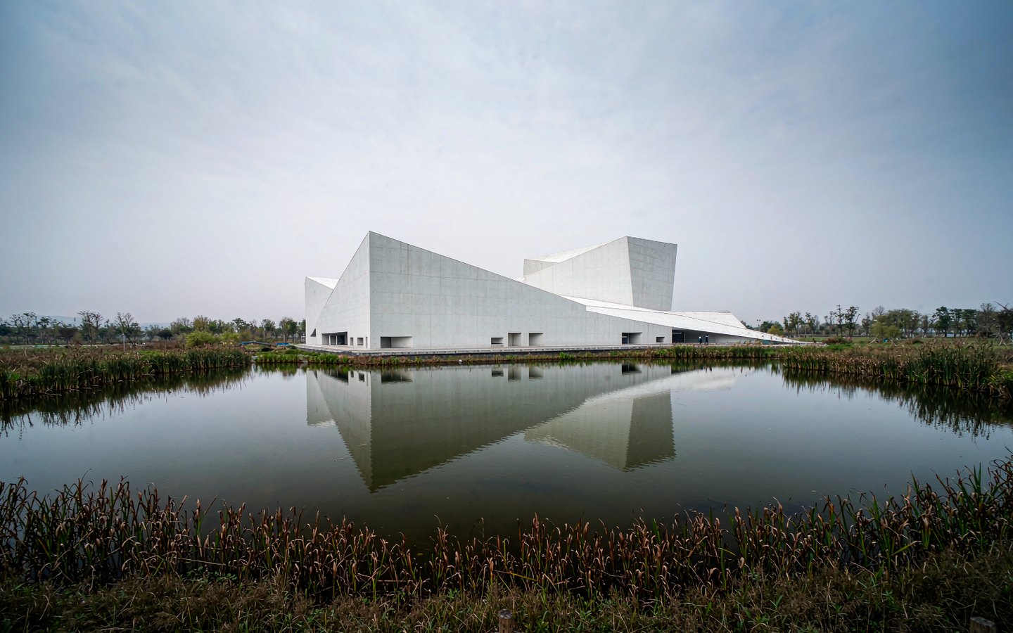 White geometric museum reflected in a calm wetland lake