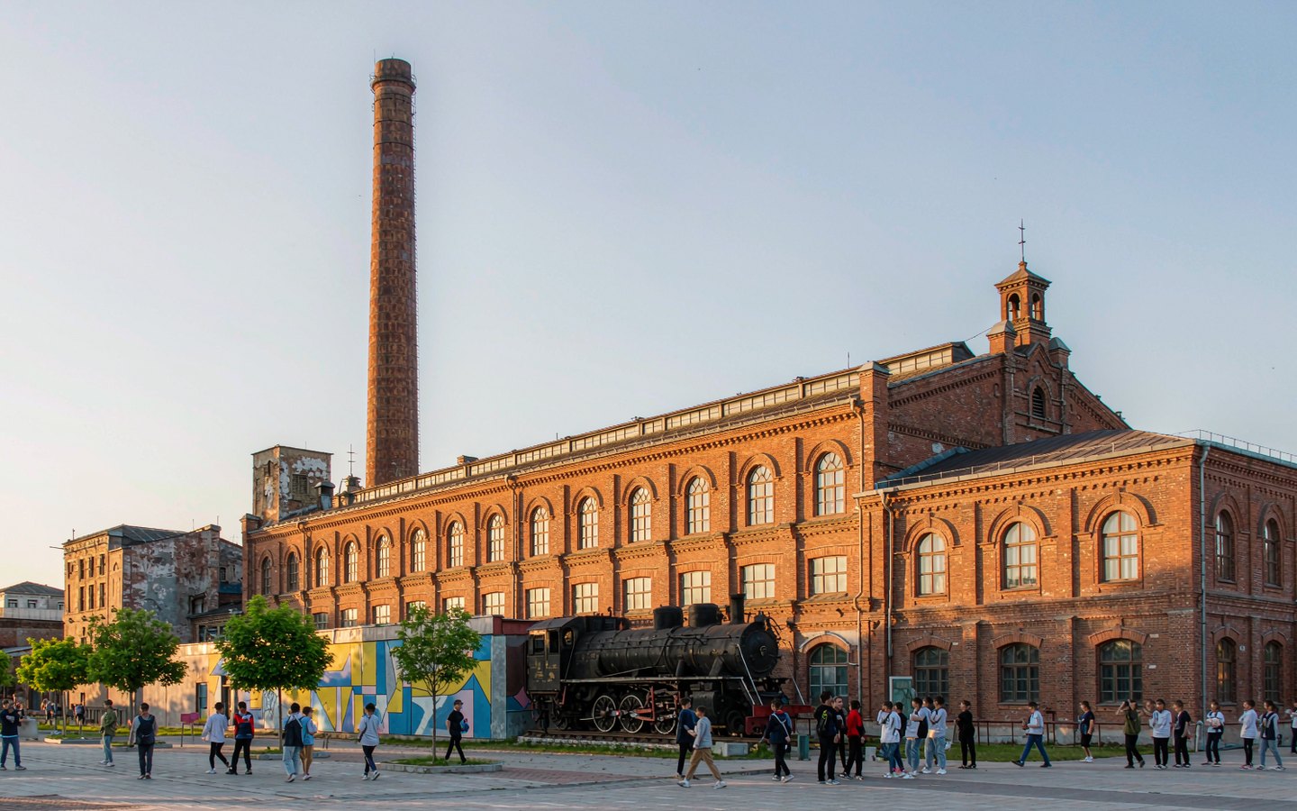 Steam locomotive beside red-brick factory halls and graffiti walls