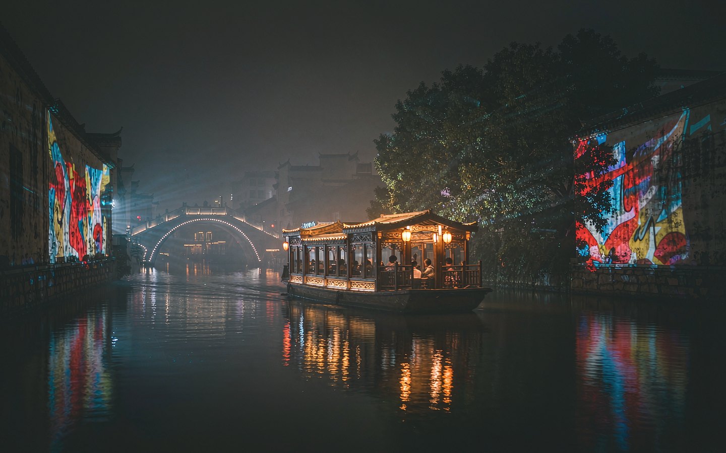 Lantern-lit covered boat gliding past light projections on old walls
