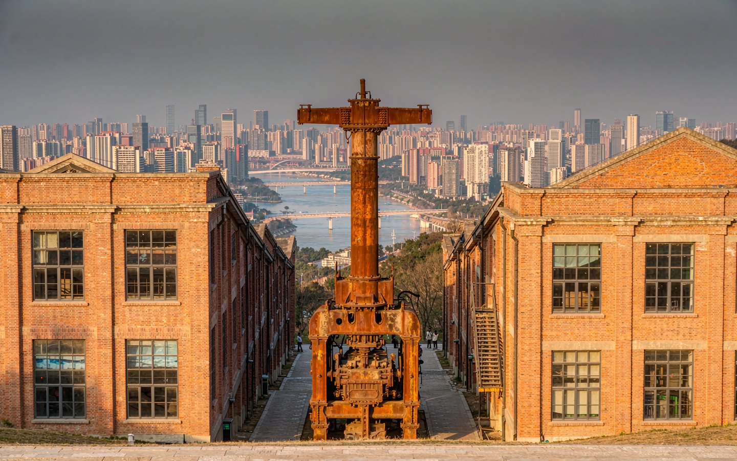 Red-brick factory lane with art installations on a hillside