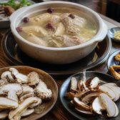 A pot of clear broth ringed by plates of raw sliced wild mushrooms