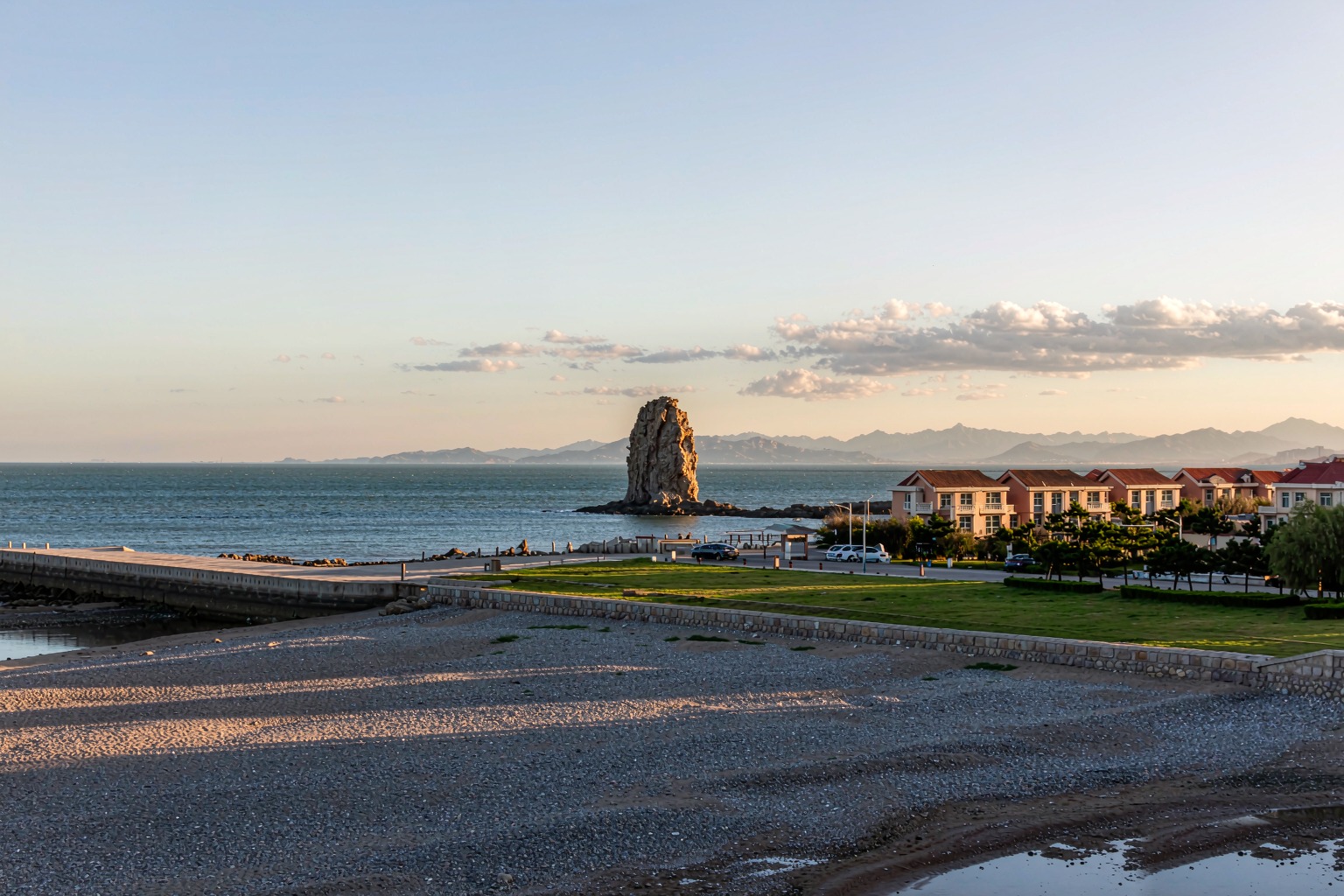 The small rocky islet of Bangchuidao seen across calm water from the pebble shore.