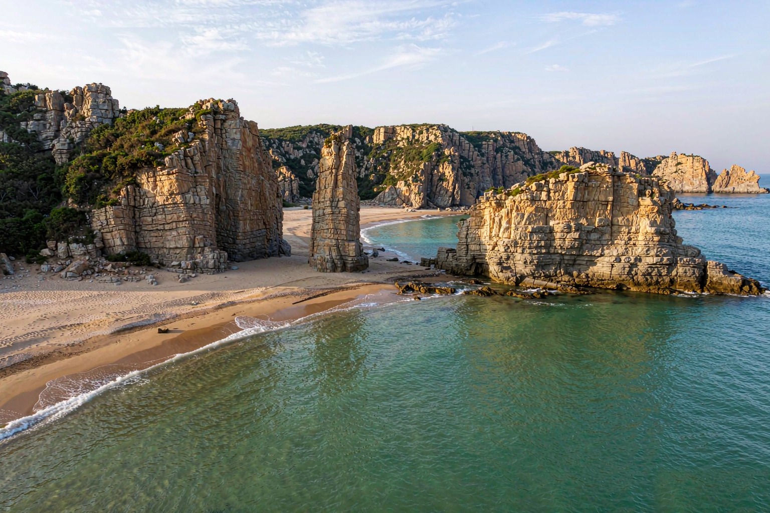 Sea-carved cliffs and clear green water at the Jinshitan national geopark coastline.