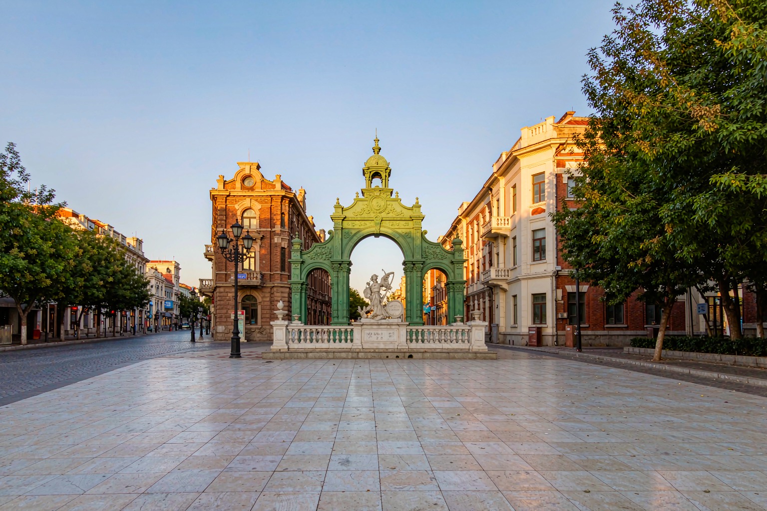 The green gate of Dalian's Russian Street glowing in late-afternoon light over the pedestrian lane.